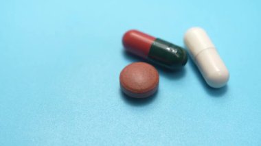 Mavi yüzeyde hap üçlüsü. Mavi bir yüzeyde kapsül ve tablet dahil üç farklı hapın videosu. Tıbbi tedavi ve farmasötik çeşitlilik kavramı.