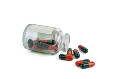 Kapsülleri dökülmüş bir şişe. Cam hap şişesi yan yatmış, kapsüller de dökülmüş. İlaç kullanımı, aşırı doz riski veya ilaç arzının sembolü.