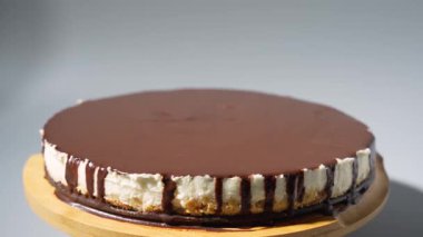 Parlak siyah çikolatayla kaplı, tahta bir tahtanın üzerinde dönen çikolatalı kek. Stüdyo çekimi pürüzsüz yüzey, kremalı katmanlar ve zarif tatlı sunumuna odaklanır..