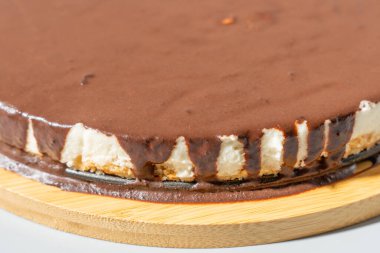 Cheesecake 'in yan görüntüsü. Kalın çikolata soslu ve görünür kremalı peynirli kekin açılı yakın çekimi. Kırsal ahşap tahta ev yapımı tatlı estetiğini geliştirir..