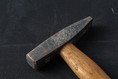 Çekiç, koyu dokulu bir yüzeyde çapraz olarak yatıyor. Yapım, onarım veya zanaat konuları için asgari endüstriyel arkaplan ideal