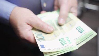 Yüzlerce avroluk banknotları sığ bir odak noktasında tutan bir elin yakın çekimi. Sahne nakit ödemeyi, kişisel finansmanı ve günlük para akışını temsil ediyor..