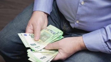 Para Yığını Tutan Adam. Günlük giysiler içindeki adam elinde kalın bir yığın 100 Euro tutuyor. Gerçekçi bir yaşam tarzında gelir, tasarruf ve kişisel finans kavramı.