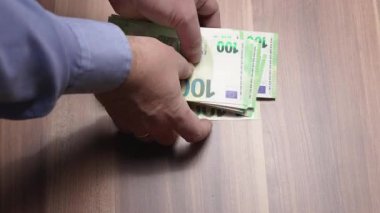 Ahşap bir masanın üzerinde bir yığın euro banknotunu el sayıyor. Nakit işleme, bütçe, zenginlik, tasarruf ve iş işlemlerini gösteren yakın plan finansal konsept.