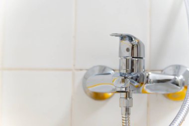 Sarı saplı bir krom musluk. Musluk bir duş başlığına bağlı.