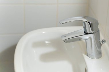 Gümüş musluğu olan bir lavabo. Musluk kapalıymış. Lavabo beyaz.