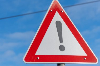 Üzerinde ünlem işareti olan kırmızı ve beyaz bir tabela. Tabela direğin üstünde.