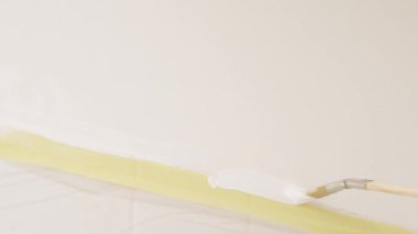 Fırça bantlı duvar boyunca taze beyaz boya sürerek keskin bir kenar oluşturur. Banyo tadilatında boyama işlemi.