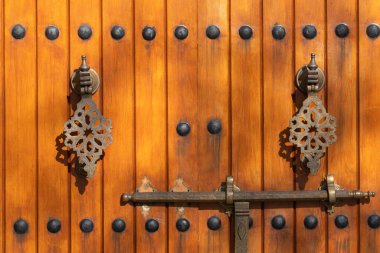 Parlak ahşap kapıdaki dekoratif metal sapların detaylı görüntüsü. Görüntü işçiliği, simetriyi ve zengin dokuları vurguluyor.