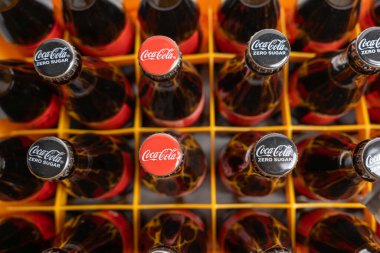 Almanya 3 Mart 2026. Sarı bir sandıkta düzenlenmiş Coca Cola şişelerinin genel bileşimi. Simetrik düzen cam ve kapakları vurguluyor..