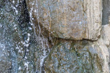 Düşen su damlacıkları bahçe şelalesinde dokulu kayalara çarpar. Sahne hareketin, ışığın ve akan suyun detaylarını vurgular..