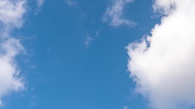 Açık mavi gökyüzü görüntüyü dolduruyor. Beyaz bulutlar yavaşça sürüklenir. Parlak gün ışığı sahneyi güçlendirir. Yumuşak bulut oluşumları derinlik katar. Huzurlu doğal ortam. Sakinleşmek için mükemmel bir ortam. Bulut zaman ayarlı.