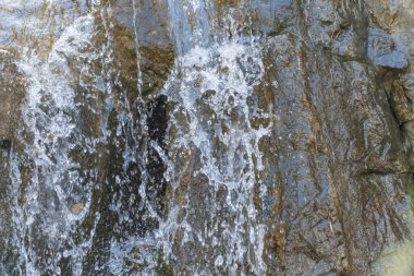 Su kayalık bir yüzeyde çağlar. Köpüklü akıntılar aşağıdaki kayaya çarpar. Karanlık ve aydınlık kayalar, akan suyla tezat oluşturur. Yakın plan suyun hareketini ve dokusunu gösterir.