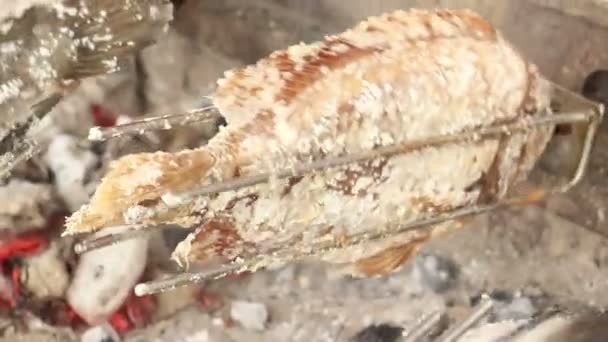 Střední boční pohled na rotující solených ryb grilování jak se otáčí nad uhlí — Stock video