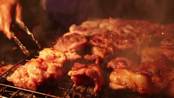 CU of an unidentified hand turning pieces of pork on a BBQ grill at night — Stock Video