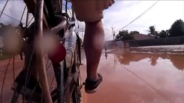 СИМ-РИП, КАМБОДИЯ - CIRCA JULY 2016: Медленное движение грязного спрея, как велосипедист в Азии проходит детей, играющих в большой луже — стоковое видео