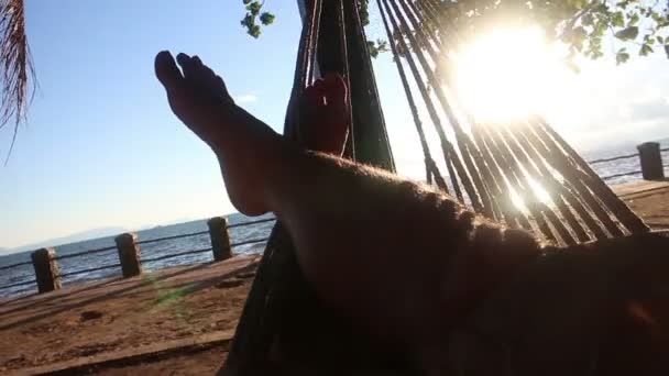 POV av personens ben i hängmatta, svängande nära havet med stark sol flimmer — Stockvideo