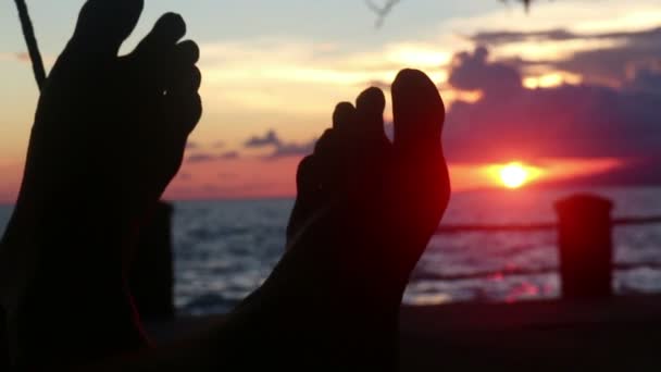 CU silueta de pies en hamaca con puesta de sol de color rojo profundo y el mar — Vídeos de Stock