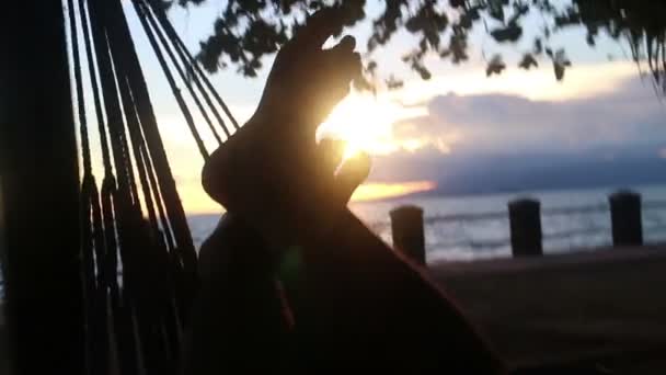 Mediano POV persona oscila moderadamente en una hamaca con puesta de sol visto entre los dedos de los pies — Vídeos de Stock