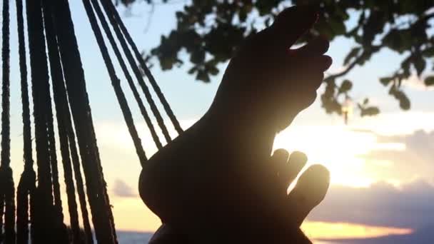 CU de los pies que balancean con la hamaca y el sol visibles detrás — Vídeos de Stock