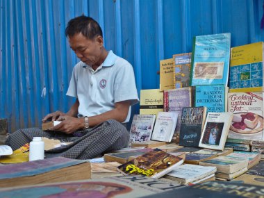 Yangon, Myanmar - 23 Aralık 2013: o bir onarım yapar gibi bir sokak kitapçı kitapları arasında oturur