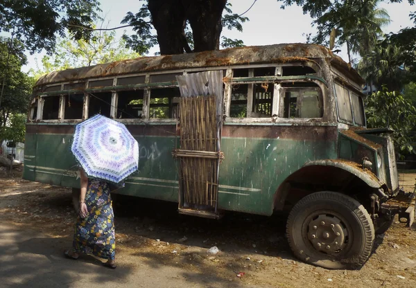 Yangon, Myanmar - April 18, 2014 - Unidentified woman with umbrellawalks past vintage dilapidated bus in Rangoon — Stock Photo, Image