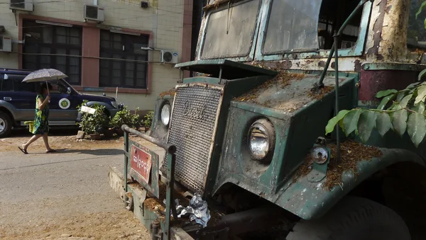 Yangon, Myanmar - 18 Nisan 2014 - kimliği belirsiz kişi şemsiye ile harap vintage yeşil otobüs ön planda geçmiş yürüyor