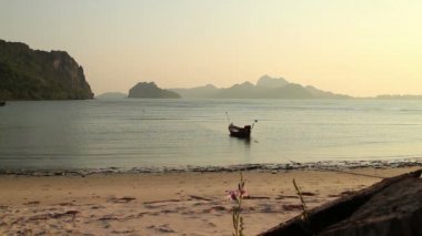 Wide shot of placid sunset bay in Southern Thailand, including a single small fishing boat moored offshore.