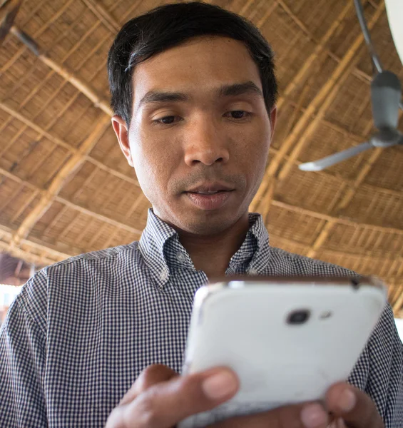 Low angle close up shot of male person of color looking at his smartphone 'Phablet' in a rustic beach cafe-like environment. — Stock Photo, Image