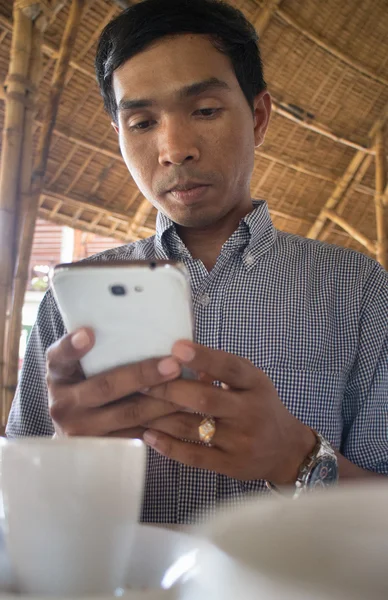 Low angle vertical medium shot of male person of color looking at his smartphone 'Phablet' in a rustic beach cafe-like environment.