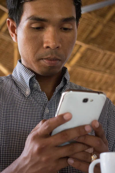 Low angle vertical medium close up shot of male person of color looking at his smartphone 'Phablet' in a rustic beach cafe-like environment.