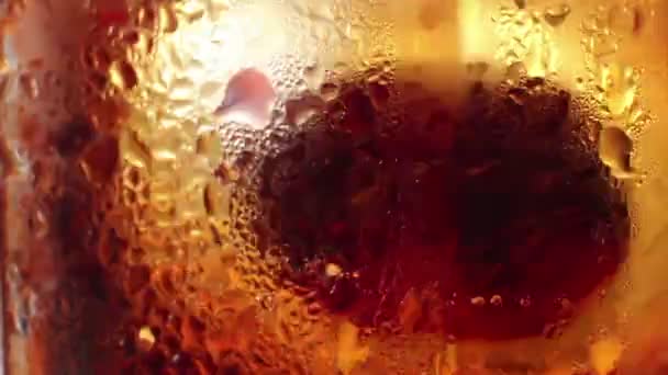 Macro ECU de hielo se agita suavemente en un vaso de líquido de color cola . — Vídeos de Stock