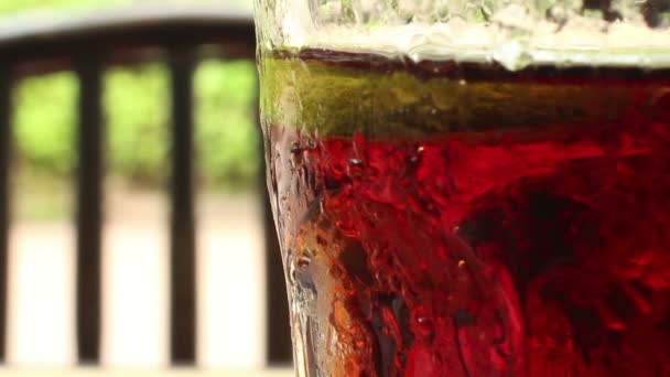 Крупным планом стакан газированного напитка цвета колы с нечетким стулом, бэкгр — стоковое видео