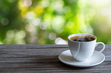 Sıcak beyaz kahve fincanı ahşap masa üstünde bulanık yeşil doğa arka planında