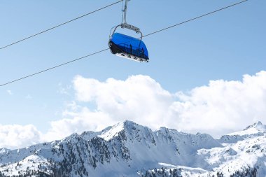 Karla kaplı dağların manzarası ve mavi koltuklu kabinleri olan teleferik. Spor, manzara, teknoloji kavramı