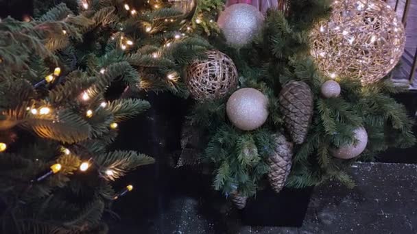 Zicht op de kerstcompositie van dennentakken, gouden ballen, kegels en een lichtgevende bloemenslinger bij de ingang van het gebouw. — Stockvideo