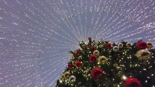 Vista de un árbol de Navidad con bolas rojas y doradas y una guirnalda brillante afuera contra el telón de fondo del cielo nocturno. — Vídeo de stock