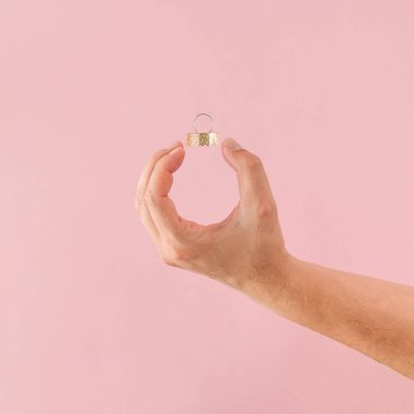 Pembe arka planda insan eli tarafından şekillendirilmiş bir Noel mücevheri. Asgari Yeni Yıl kavramı.