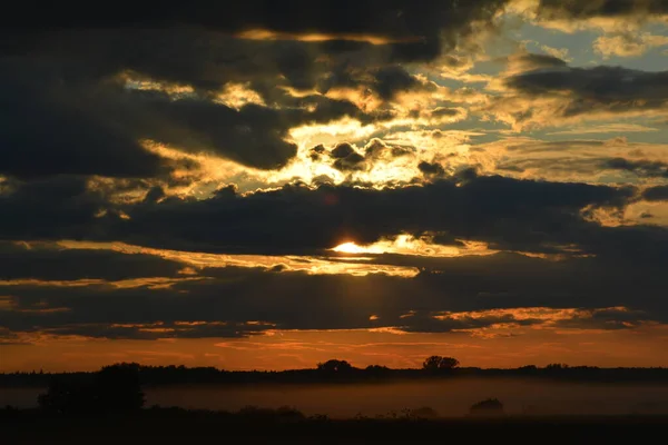 A July summer evening. The sun is setting below the horizon. The fog rises from the river. Sunset and clouds.