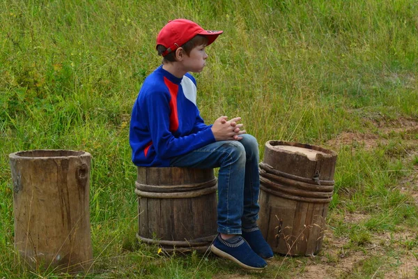 The boy was tired and sat down to rest on an old tub. Varankiny village, Afanasyevsky district, Kirov region, Russia. July 2021. Nikon D 5200.