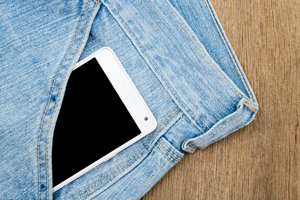 White smart phone in jeans pocket on wooden background.