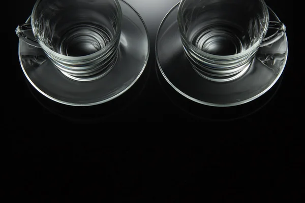 Dvě skleněné, šálek na čaj a prázdný talířek na černém pozadí — Stock fotografie