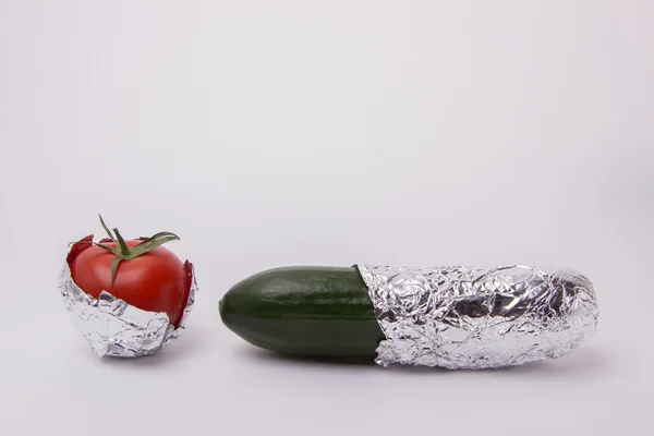 Pepino verde y tomate envueltos en papel de aluminio sobre un fondo blanco — Foto de Stock