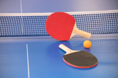 Masa tenisi için turuncu top ve iki ahşap raket kırmızı ve siyah renkli bir masa üzerinde ızgara ile