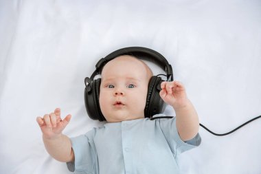 Sevimli güzel bebek gülümser ve siyah kulaklıklarla beyaz arka planda müzik dinler. Çocuk eğitimi. 