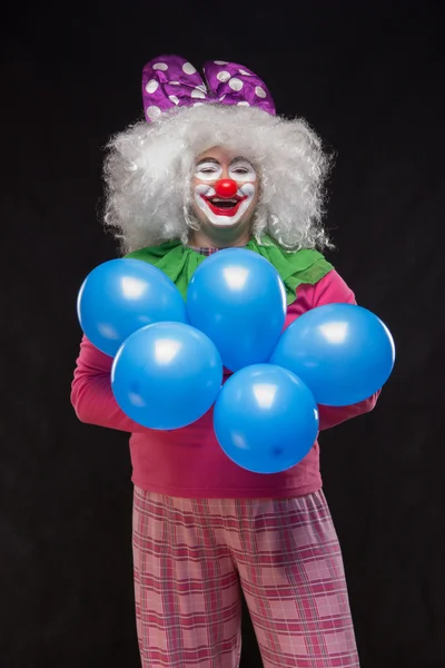 Funny clown with shaggy hair holding colorful balloons on a blac — Stock Photo, Image