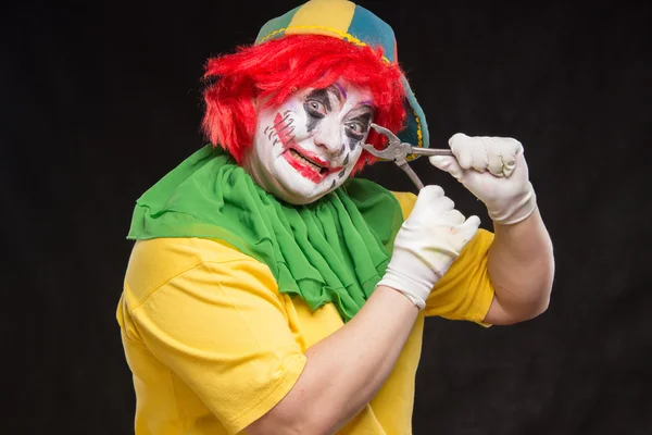 Scary evil clown with an ugly smile and a pair of pliers on a bl — Stock Photo, Image
