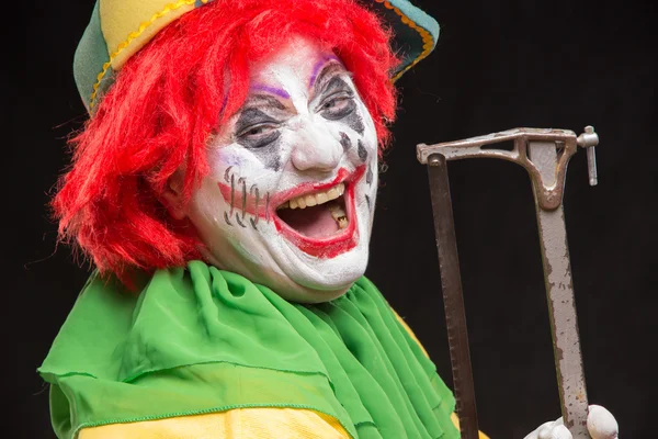 Scary evil clown with an ugly smile and saw on a black backgroun — Stock Photo, Image