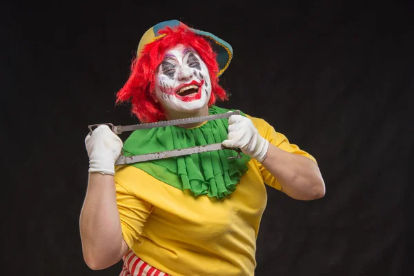 Scary evil clown with an ugly smile and saw on a black backgroun — Stock Photo, Image
