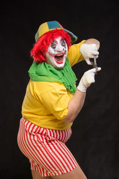 Scary evil clown with an ugly smile and a pair of pliers on a bl — Stock Photo, Image